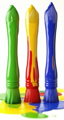 Three paintbrushes, green, yellow, and blue, dripping with colorful paint