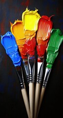 Five paintbrushes, dripping with vibrant primary and secondary colors, against a dark background