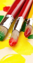 Close-up of three paintbrushes with colorful paint on a canvas