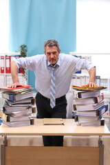 Office worker in shirt and tie stands in the office in front of stacks of files and looks very...