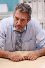 Office worker in shirt and tie sits in the office and looks annoyed