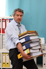 Office worker in shirt and tie carries a heavy stack of files, looks strained