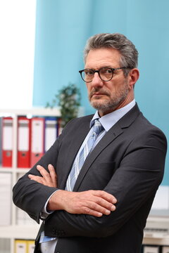 Office worker with glasses and suit has his arms crossed in front of his body and looks sternly and dominantly to the side