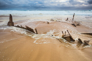 Waves recede over scrap metal pieces of a shipwreck on a beach