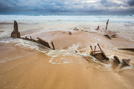 Waves recede over scrap metal pieces of a shipwreck on a beach