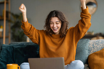 Happy woman sitting on sofa with laptop, raising arms in victory and celebrating after winning online competition or lottery. Joy, success, and digital lifestyle concept.

