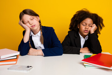 Two schoolgirls in uniforms seemingly tired, resting during a study session, highlighted by a...