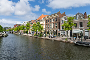 Fototapeta premium Beautiful canal scene in Leiden, Netherlands, featuring historic gabled houses, tree-lined quays, and a tranquil waterway. Perfect for travel, European architecture, and Dutch culture themes.