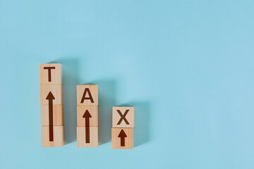 Wooden blocks with arrows spelling TAX are arranged in descending stacks, conceptualizing a tax...