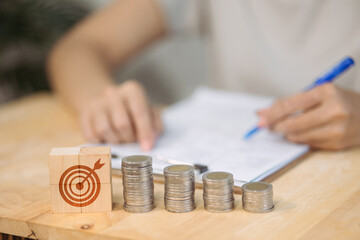Fototapeta premium Wooden blocks forming a target symbol are placed next to descending stacks of coins, representing the focus on achieving financial goals.
