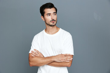 Thoughtful young caucasian man with stylish haircut wears white t-shirt standing against gray...