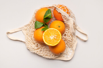 Ripe juicy oranges in cotton string bag on light gray background top view flat lay. Eco-friendly...