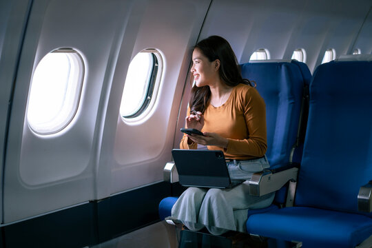 woman is sitting on a blue airplane seat with a laptop open in front of her - Powered by Adobe