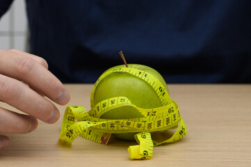 Restrictive weight loss diet, green apple wrapped in a measuring tape on the table