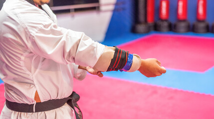 Close-up of a martial arts practitioner adjusting an arm guard over his white uniform. The person...