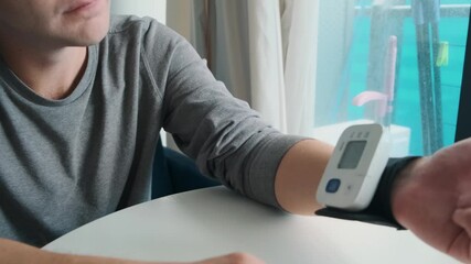 Man using digital wrist blood pressure monitor for measuring blood pressure and pulse at home. Technology for regular health tracking. Managing hypertension, heart health and general wellness - Powered by Adobe