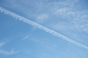 A clear blue sky with soft clouds and distinct plane tracks streaking across, creating a minimalist...