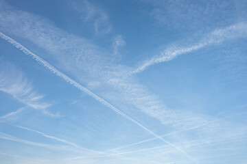 A clear blue sky with soft clouds and distinct plane tracks streaking across, creating a minimalist yet dynamic composition. A serene and airy view of the open sky.