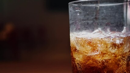 Bubbling carbonated drink is poured in a glass full of ice.