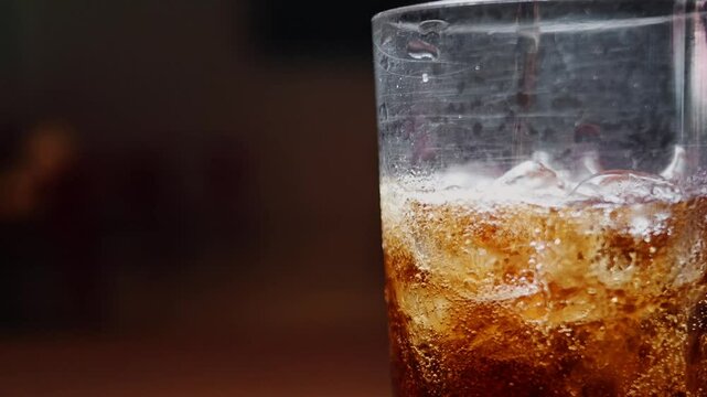 Bubbling carbonated drink is poured in a glass full of ice. - Powered by Adobe