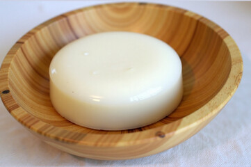 A round piece of cheese sitting in a wooden bowl.