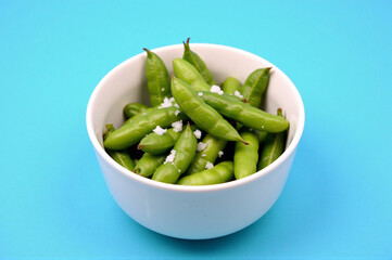A white bowl filled with green beans on a blue background.
