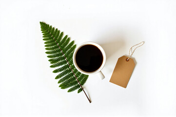 A cup of coffee and a fern leaf on a white surface.