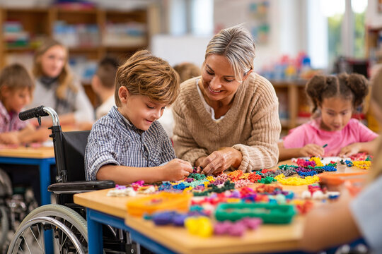 Teacher assists children in wheelchairs as an AI device creates colorful plasticine objects on their desks in a classroom. Inclusive, creative, and technology-driven learning environment.

