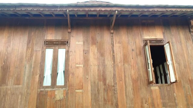 Traditional wooden house wall with two windows one window open in drizzling atmosphere