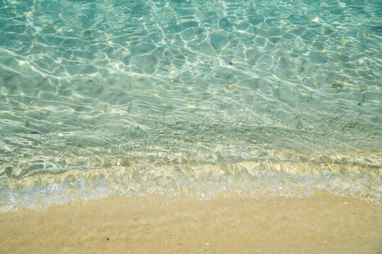 Close up of blue sea water and a small wave bubbling onto a beach