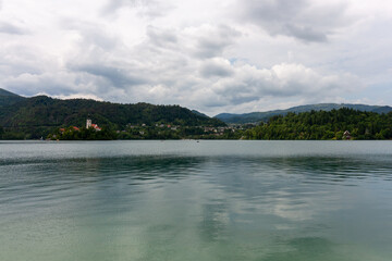 A picturesque view of Lake Bled is framed by lush green foliage in the foreground, offering a glimpse of the serene turquoise waters