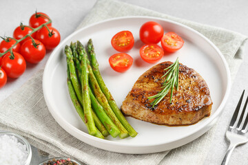 Close up, macro of tasty grilled beef steak served with green asparagus and cherry tomatoes on white plate, with cutlery. Perfect for food menu, diet, or culinary design concepts.