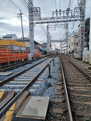 Fototapeta premium Railway Tracks in Suburban Japan with Overhead Wires and Residential Buildings on a Cloudy Day
