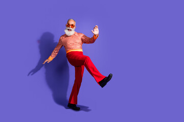 Happy senior man wearing retro clothing, posing confidently in a dynamic dancing gesture on a vibrant purple background