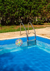 Playful inflatable ball in swimming pool, positioned across from metal ladder. Lighthearted summer...