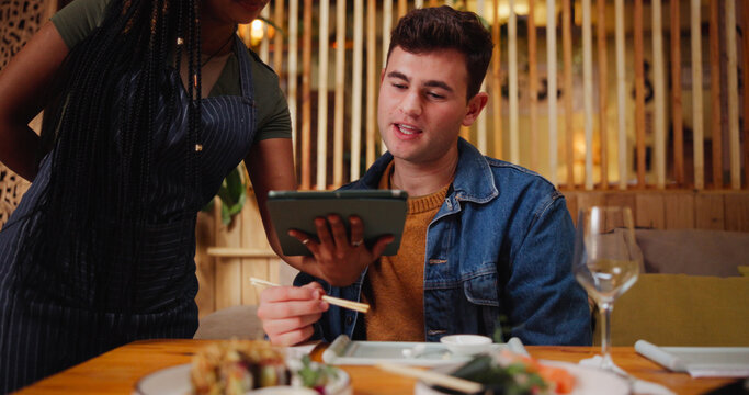 Man, customer and waitress with tablet at restaurant for menu, order price and reading information. People, server and digital for food choice, sushi selection and hospitality service for lunch date