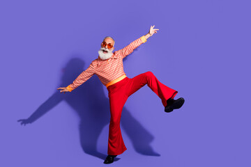Stylish senior man dancing energetically in vibrant vintage retro attire against purple background