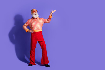 Stylish senior man in vibrant retro clothing posing energetically against a purple backdrop