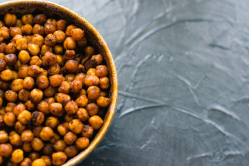 Delicious snack, fragrant baked with spices chickpeas in a brown bowl on a dark background with...