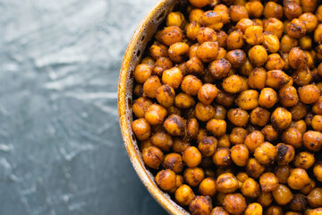 Delicious snack, fragrant baked with spices chickpeas in a brown bowl on a dark background with...