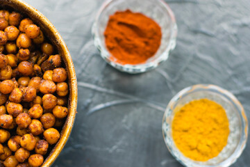 Delicious snack, fragrant baked with curry spices and smoked paprika chickpeas in a brown bowl and spices on a dark background with space for text. Healthy eating concept.