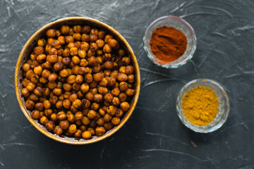 Delicious snack, fragrant baked with curry spices and smoked paprika chickpeas in a brown bowl and spices on a dark background with space for text. Healthy eating concept.
