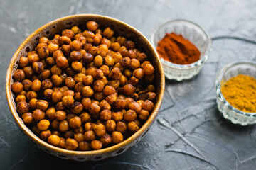 Delicious snack, fragrant baked with curry spices and smoked paprika chickpeas in a brown bowl and spices on a dark background with space for text. Healthy eating concept.