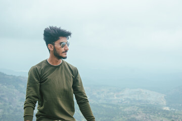 A young man in a green sweater contemplates the panoramic view from Nandi Hills, Bengaluru,...