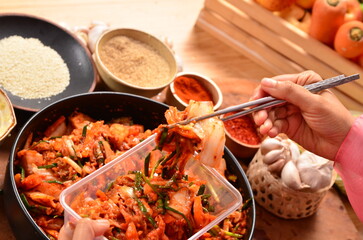picks up kimchi in a plastic container with chopsticks from a bowl of shredded vegetables,...
