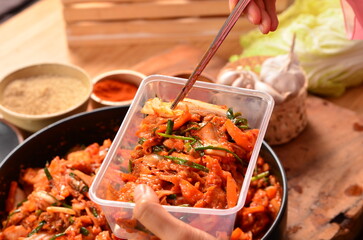 picks up kimchi in a plastic container with chopsticks from a bowl of shredded vegetables,...