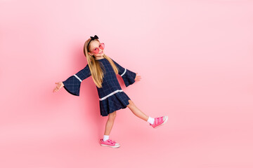 Adorable young girl wearing stylish outfit and posing playful against pink background