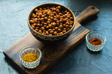 Delicious snack, fragrant baked with curry spices and smoked paprika chickpeas in a brown bowl and spices on a dark background with space for text. Healthy eating concept.