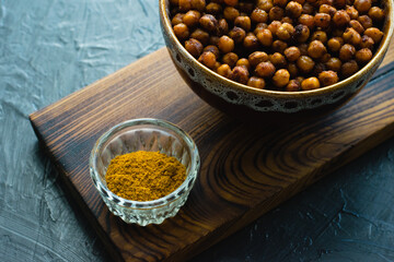 Delicious snack, fragrant baked with curry spices and smoked paprika chickpeas in a brown bowl and spices on a dark background with space for text. Healthy eating concept.