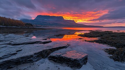 Fototapeta premium Dramatic sunrise over a fjord. Rocky shoreline reflects vibrant sunset colors